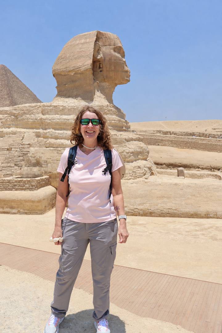 Traveler poses near ancient stepped limestone blocks of Egypt's Saqqara complex under a clear sky.