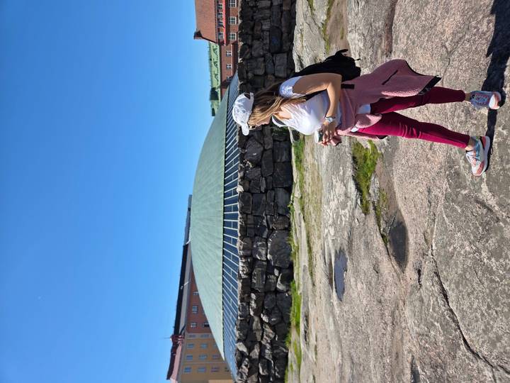 Traveler looks toward the green domed rock-hewn Temppeliaukio Church set against a clear blue sky.