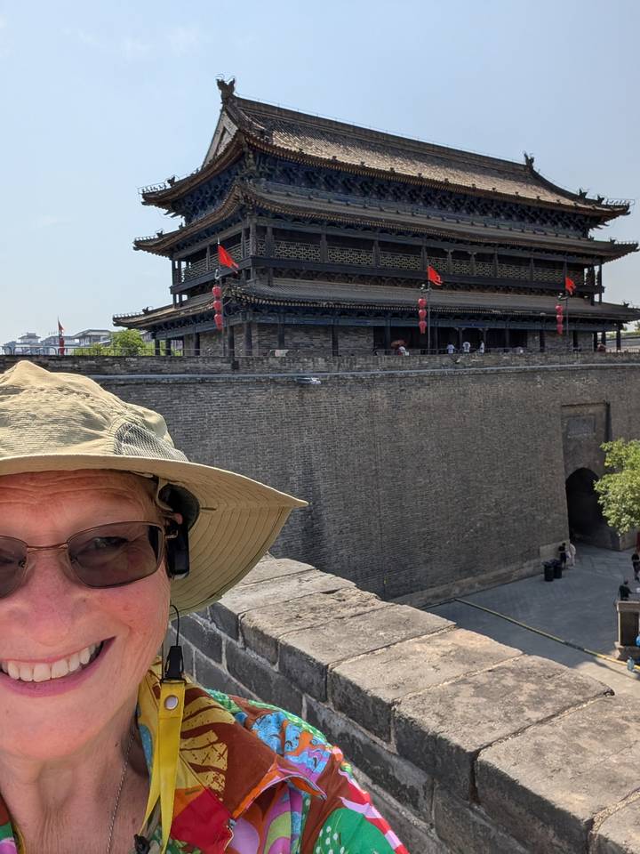 Partial selfie in sunhat with ancient Xi'an city wall tower and red lanterns behind.