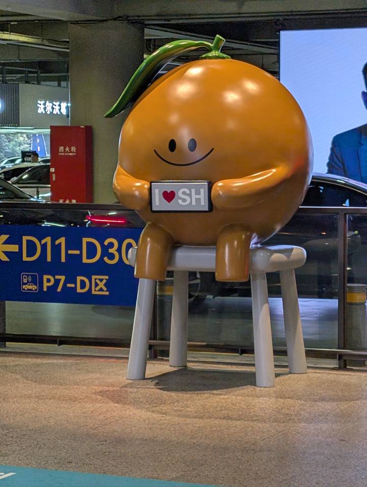 Cute round mascot statue holding an 'I ♥ SH' sign inside an urban terminal.