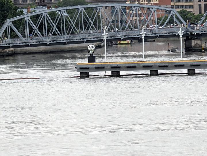 Wide river scene with iron bridge and a panda figure statue on the pier.