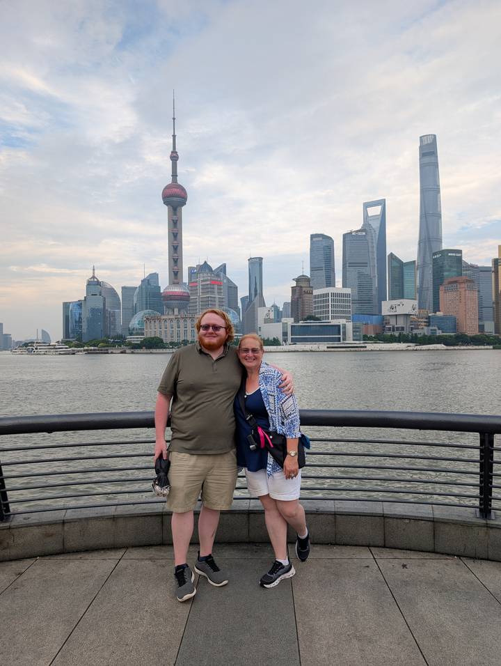 Smiling couple on the Shanghai Bund with iconic skyline and Oriental Pearl Tower across the Huangpu River.