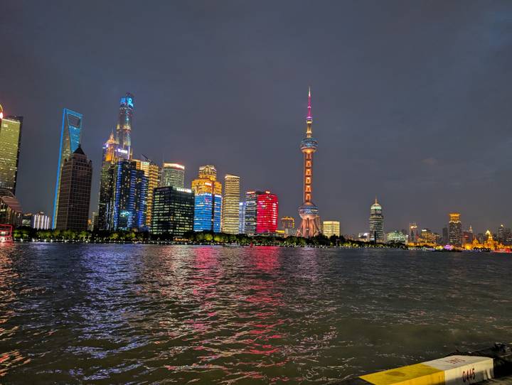 Night view of illuminated Shanghai skyline reflecting vibrant colors onto the Huangpu River.