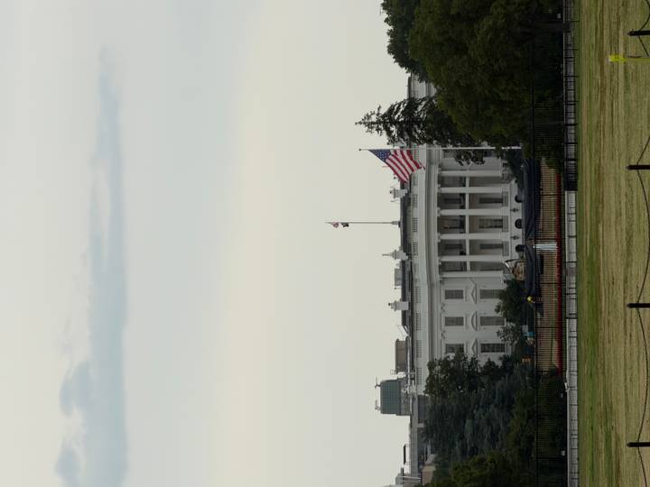Distant view of the White House with American flag flying at half-mast on a calm day.