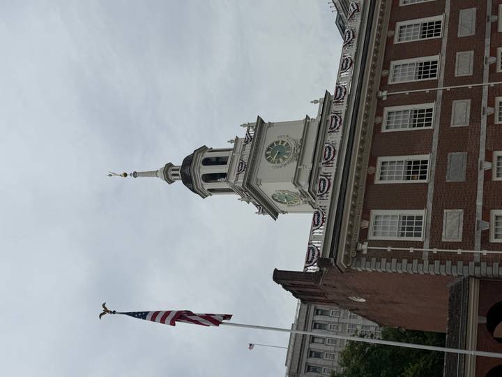 Clock-towered facade of Independence Hall with an American flag against an overcast sky.