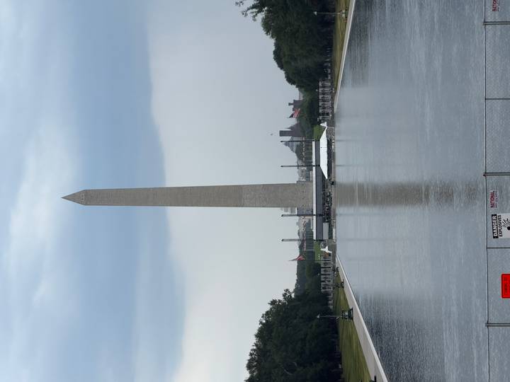 Tall Washington Monument reflected in the still water of the Reflecting Pool under a cloudy sky.