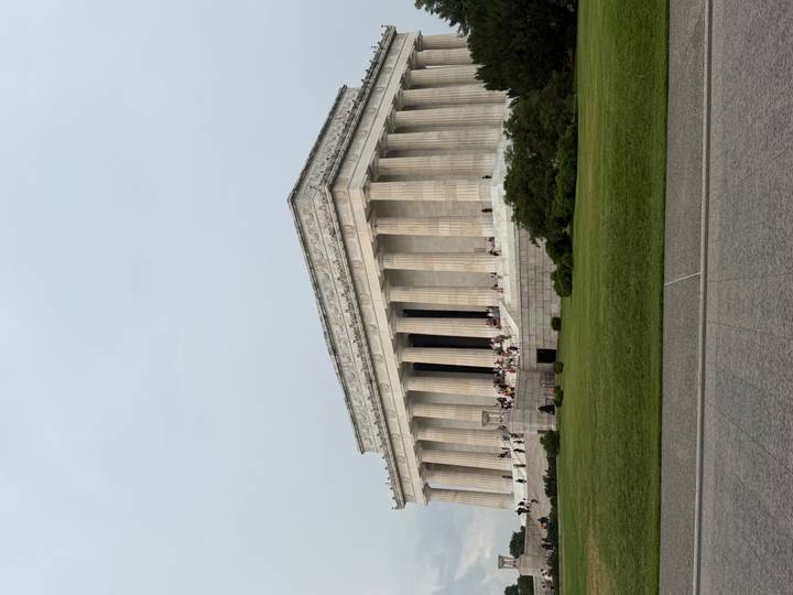 Exterior view of the columned Lincoln Memorial with visitors on the steps and manicured lawns in front.