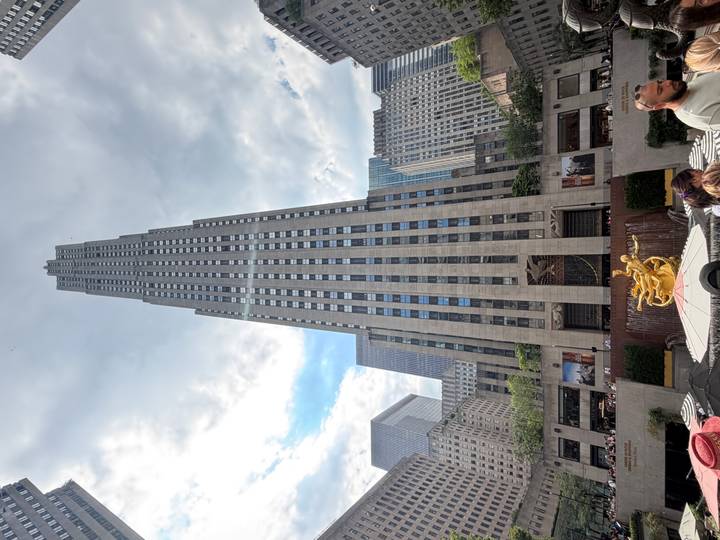 Rockefeller Center skyscraper soaring upwards with Prometheus statue and plaza crowds below.