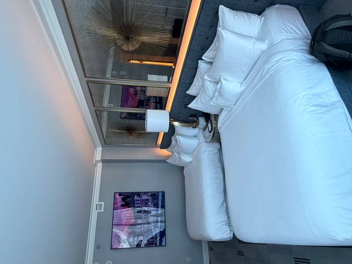Modern hotel room with two large neatly made beds, soft lighting and framed artwork on the wall.
