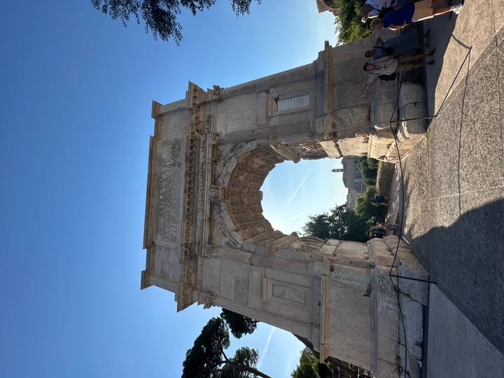 Majestic ancient Roman arch monument towering against a clear blue sky with visitors below.