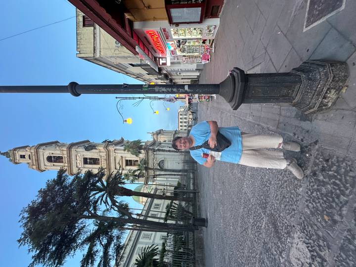 Woman posing on a cobblestone street near a tall bell tower at dusk with streetlights on.