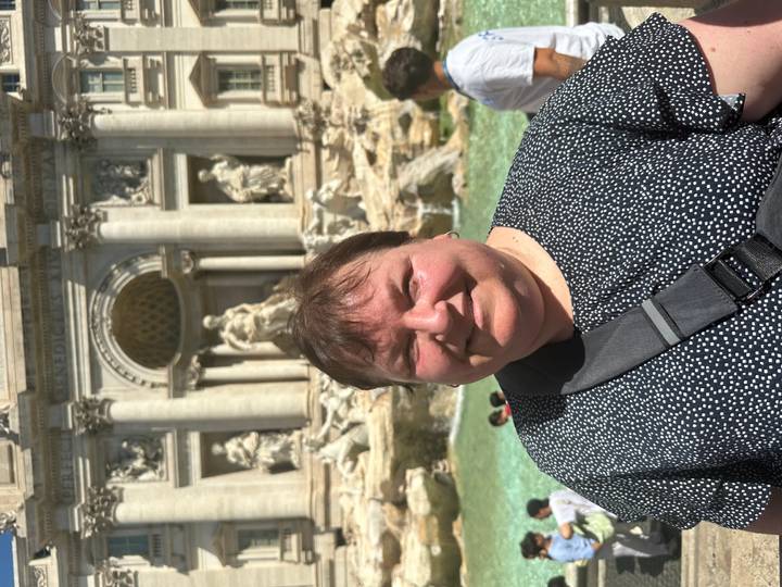 Portrait of a woman smiling in front of the statues and water of Trevi Fountain.