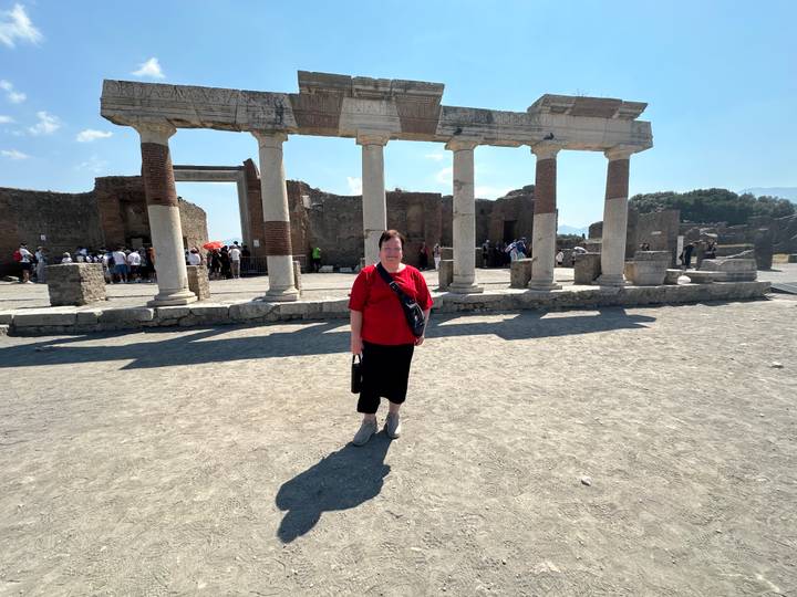 Woman poses in front of columned ruins on the dusty ground of Pompeii archaeological site.