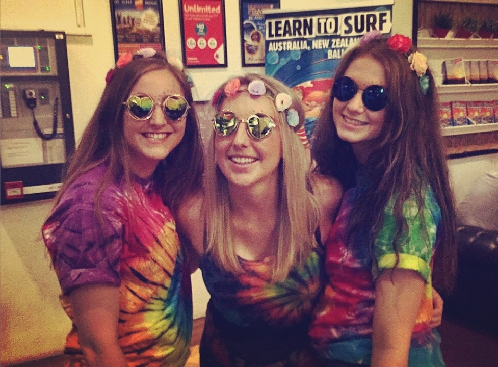 Three people posing indoors wearing tie-dye clothing.