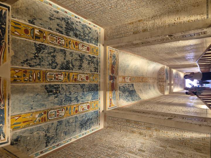 Upward view of vivid hieroglyphic ceiling panels and walls as tourists photograph inside an Egyptian tomb.