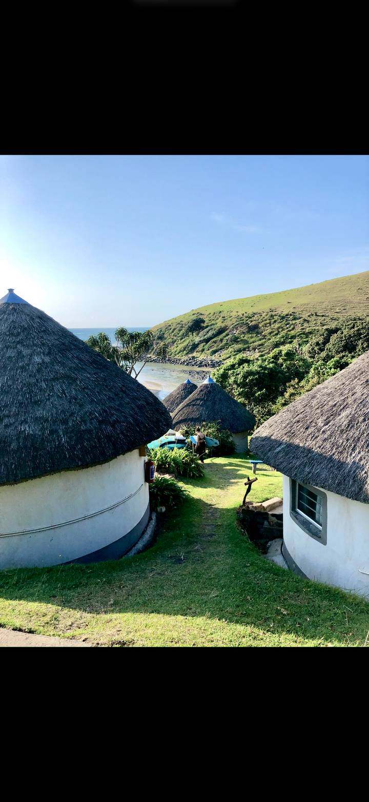 Thatched rondavel cottages surrounded by lush greenery above a tidal estuary on a sunny afternoon.