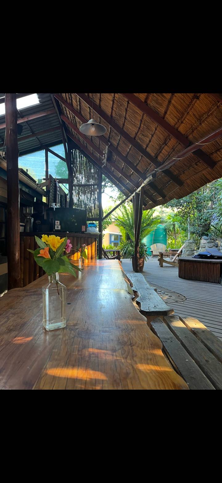Open-air lodge deck with wooden tables, flower vase, and lush tropical garden beyond.