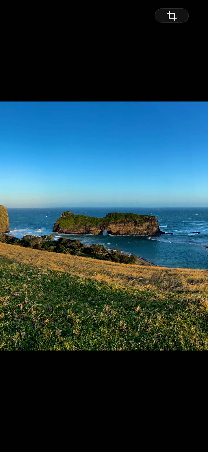 Dramatic sea stack known as Hole-in-the-Wall stands in turquoise waves beneath a clear blue sky.