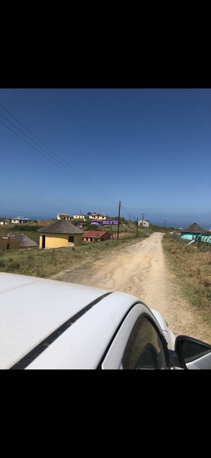 Dusty rural road leading to colorful round huts scattered across a hillside with power lines above.