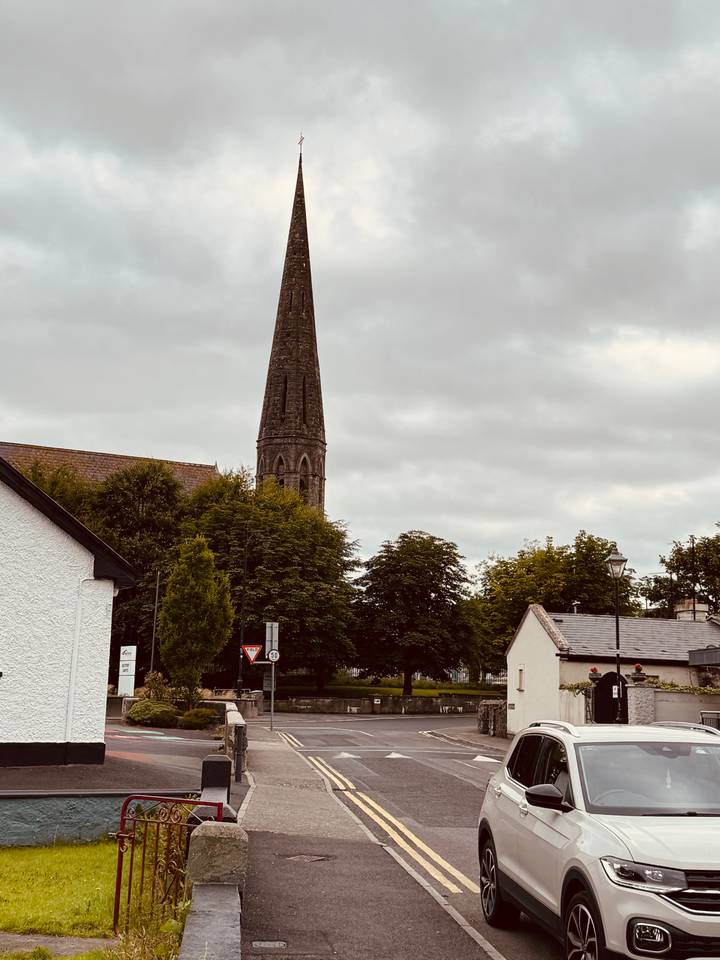 Tall church steeple rises above trees and village houses beneath a grey overcast sky.