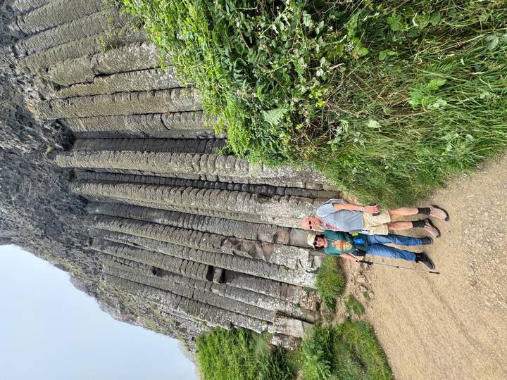 Two hikers stand beside towering hexagonal basalt columns at Giant's Causeway.