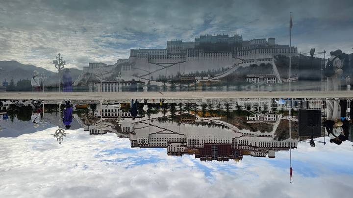 Potala Palace majestically reflected in a still pool under a textured sky.