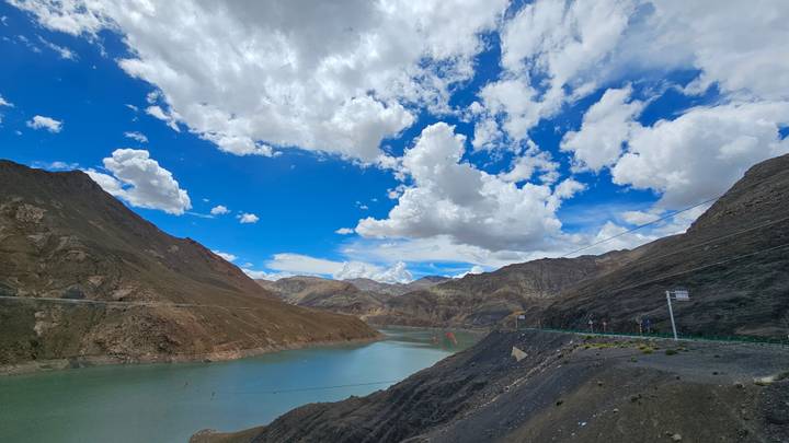 Turquoise high-altitude lake surrounded by arid brown mountains beneath scattered clouds.