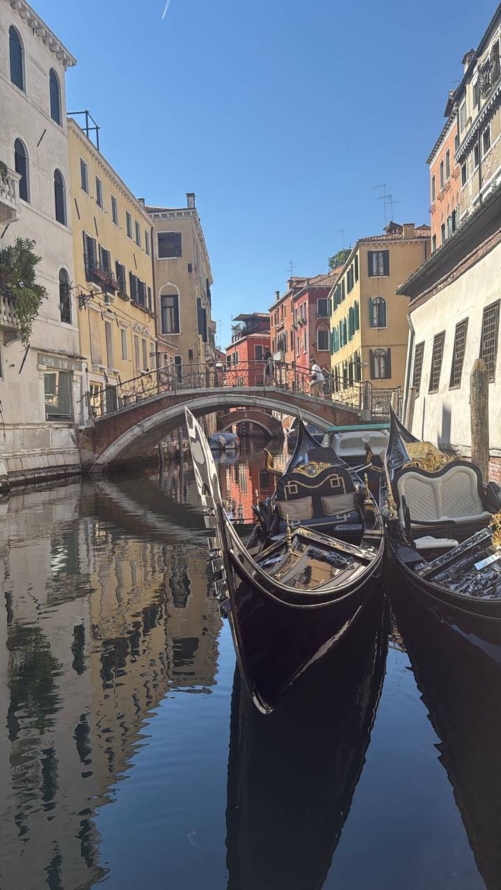 Moored gondolas beside a quaint stone bridge reflecting in a calm Venetian canal.