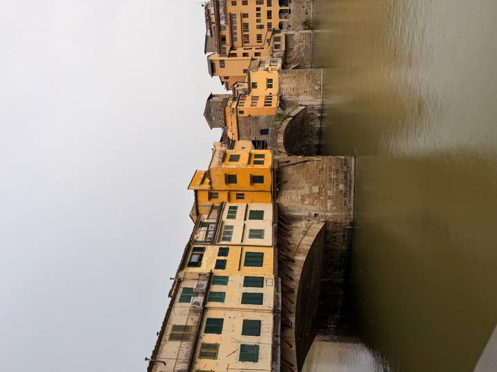 The historic Ponte Vecchio bridge spans the Arno River with its yellow and orange buildings.