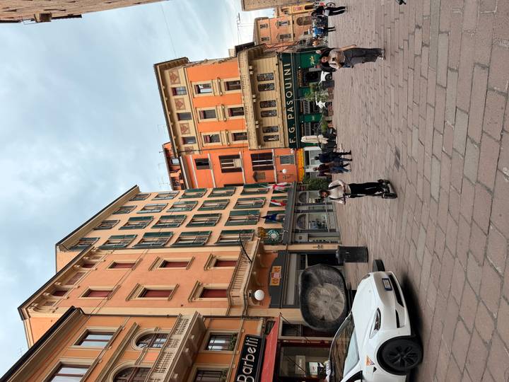 People stroll and a rider on an e-scooter passes through a colourful piazza in Bologna.
