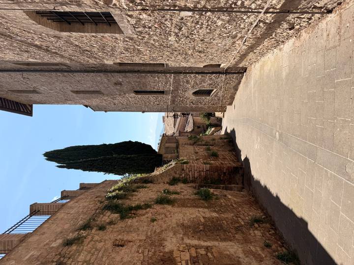 A quiet stone alleyway slopes downward between historic buildings under clear blue sky.