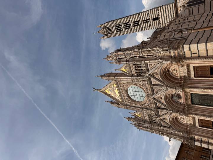 The ornate façade of Siena Cathedral rises into a blue sky with golden mosaics catching the light.