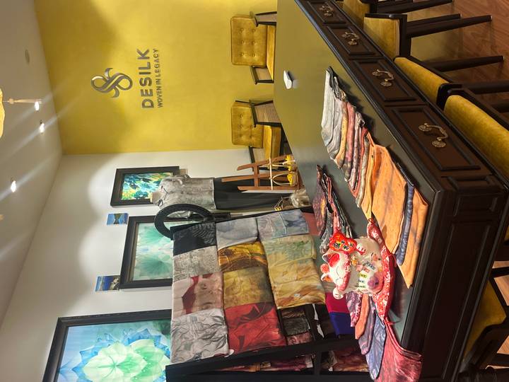 A boutique showroom with colorful silk scarves laid out on a dark wooden table against a bright yellow wall labeled DESILK.
