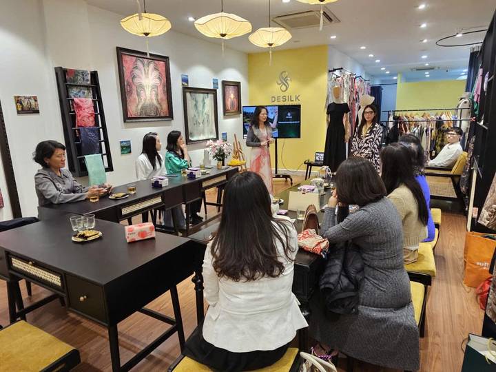 Visitors sit around tables inside a silk boutique while listening to a presentation on traditional textiles.