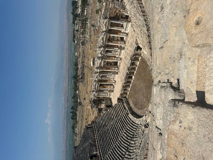 Panoramic view of the ancient Roman theatre at Hierapolis with sweeping stone tiers and colonnaded stage set against distant mountains.