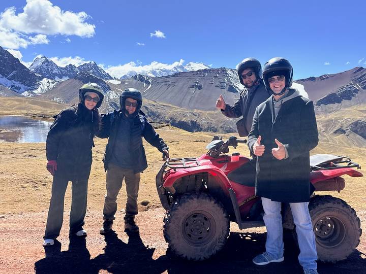 Travellers in helmets give thumbs up beside an ATV with snow-capped Andes peaks behind.