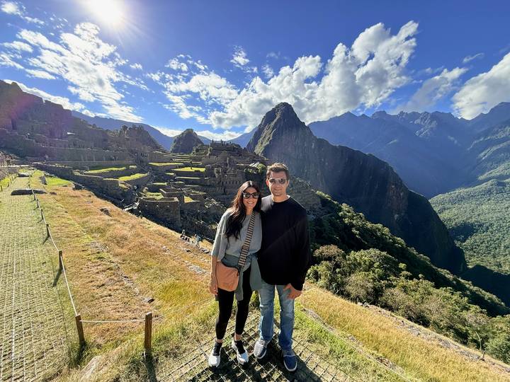 A couple poses at the classic postcard viewpoint overlooking Machu Picchu with jagged peaks behind.
