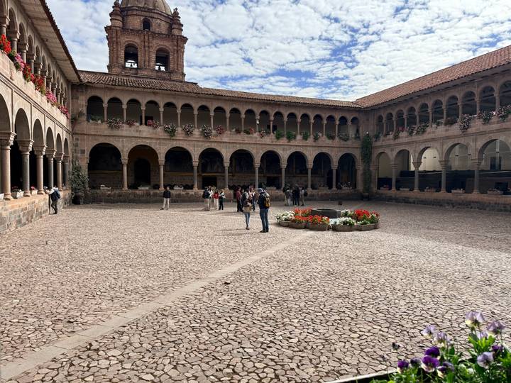 Visitors explore the cobblestone courtyard of Qorikancha monastery with arch colonnades in Cusco.