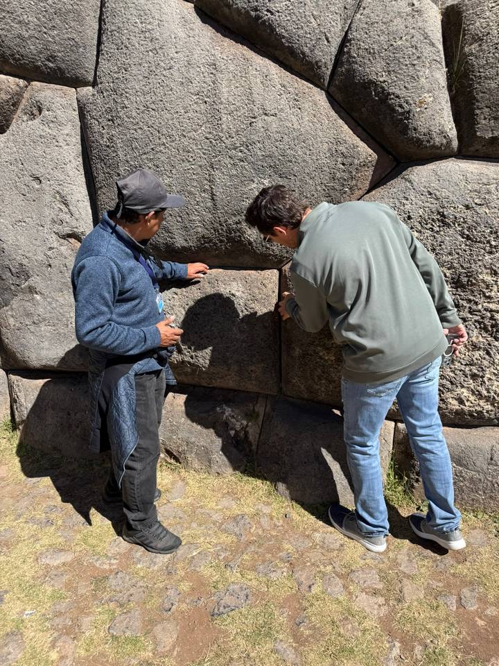 Guide explains precise Inca stonework to a visitor at Sacsayhuamán wall in Cusco.