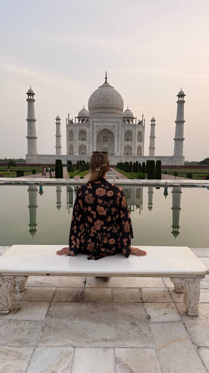 Woman in floral robe admires the Taj Mahal reflected in the silent pool at dawn.