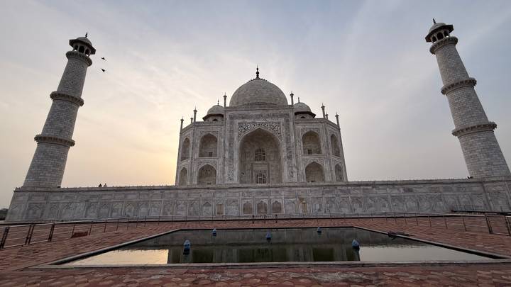 Silhouetted view of the Taj Mahal with soft sunset light behind its white marble façade.