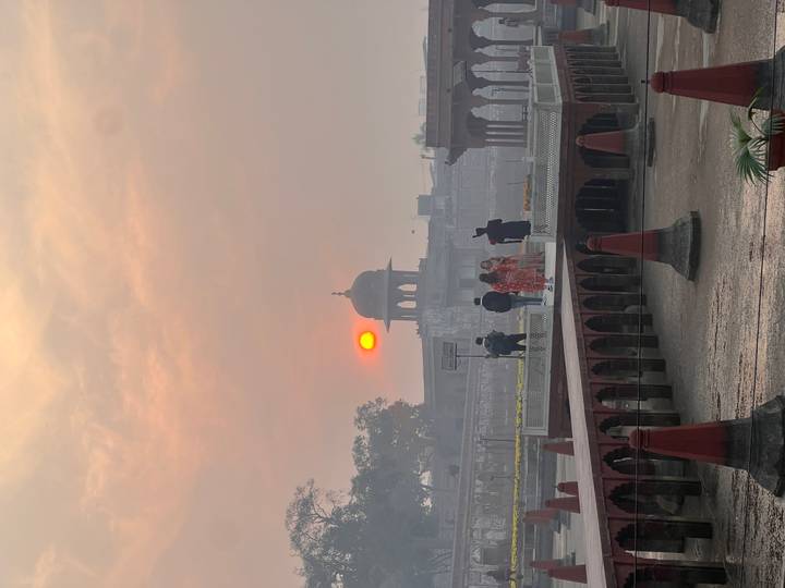 Sunset scene at Lahore Fort pavilion with silhouettes of visitors and orange sun.