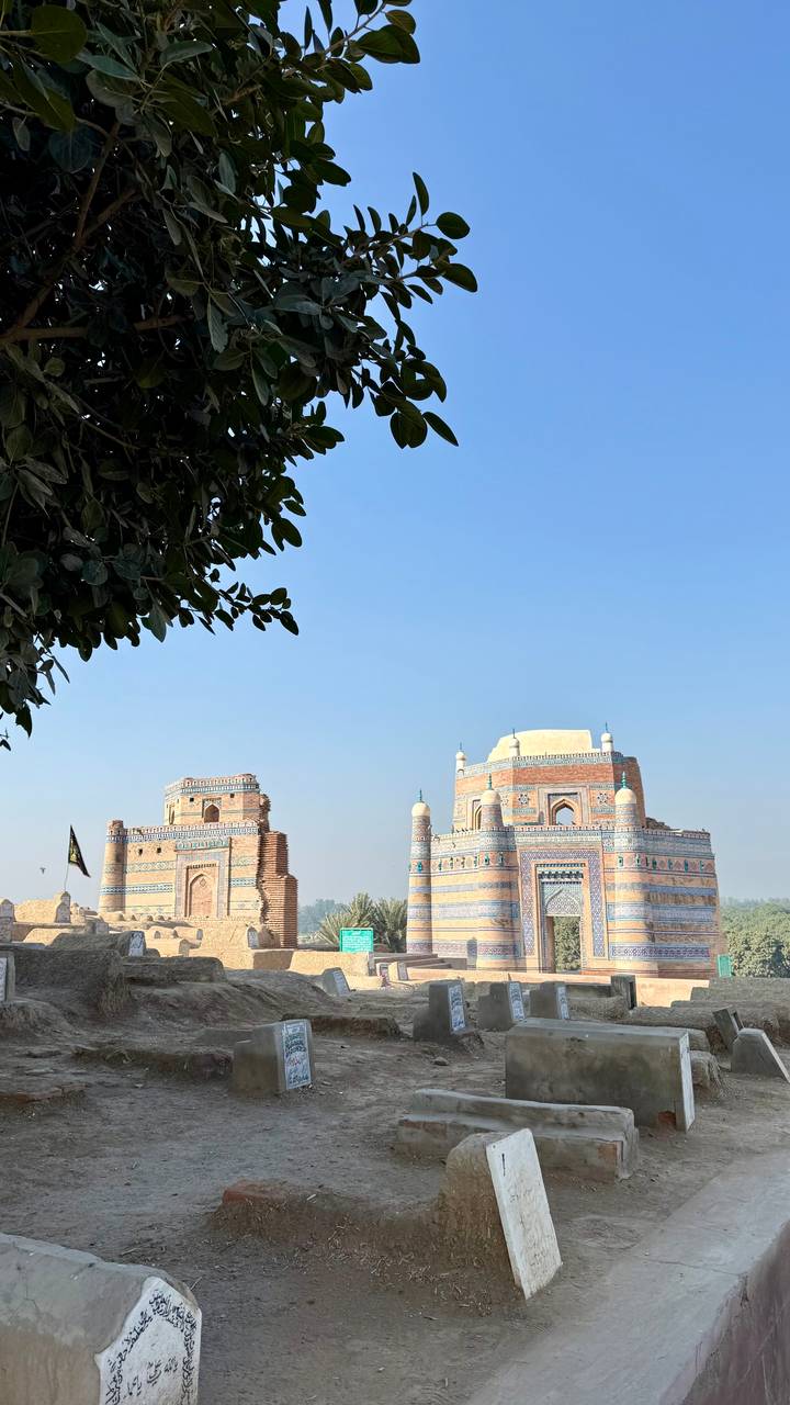 Twin blue-tiled gateway towers of a Sufi shrine under clear sky.