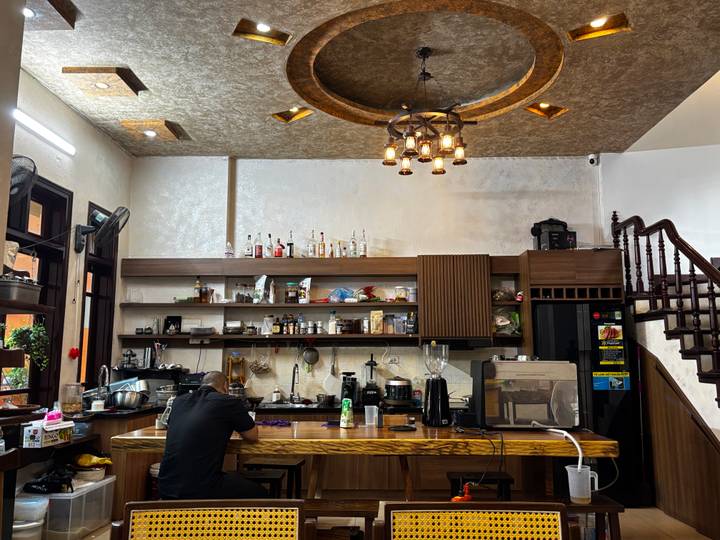Cozy café interior with a man sitting at the wooden bar surrounded by coffee equipment and shelves.