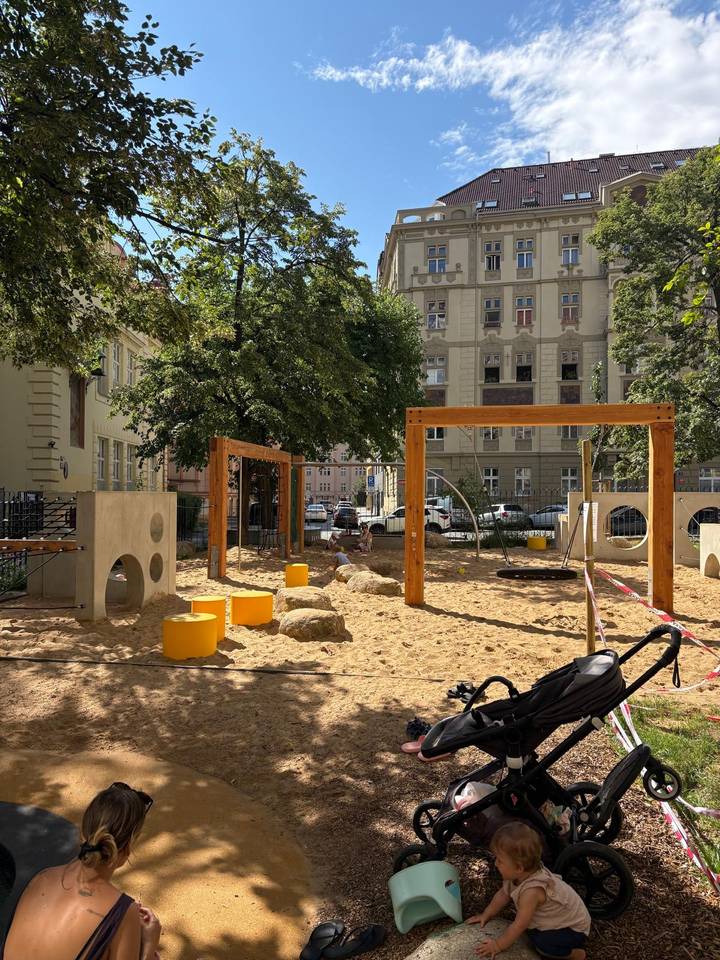 Urban playground with sand, climbing frames and a child playing surrounded by historic apartment buildings.