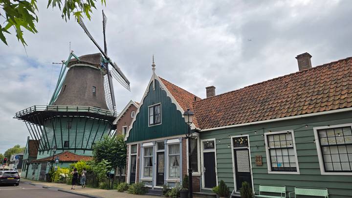 Traditional green wooden houses and a large historic windmill under a cloudy sky in Zaanse Schans.