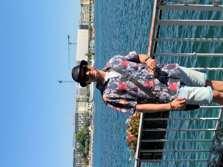 Full-body portrait of a traveller by the Geneva lakeside railing on a bright summer day.