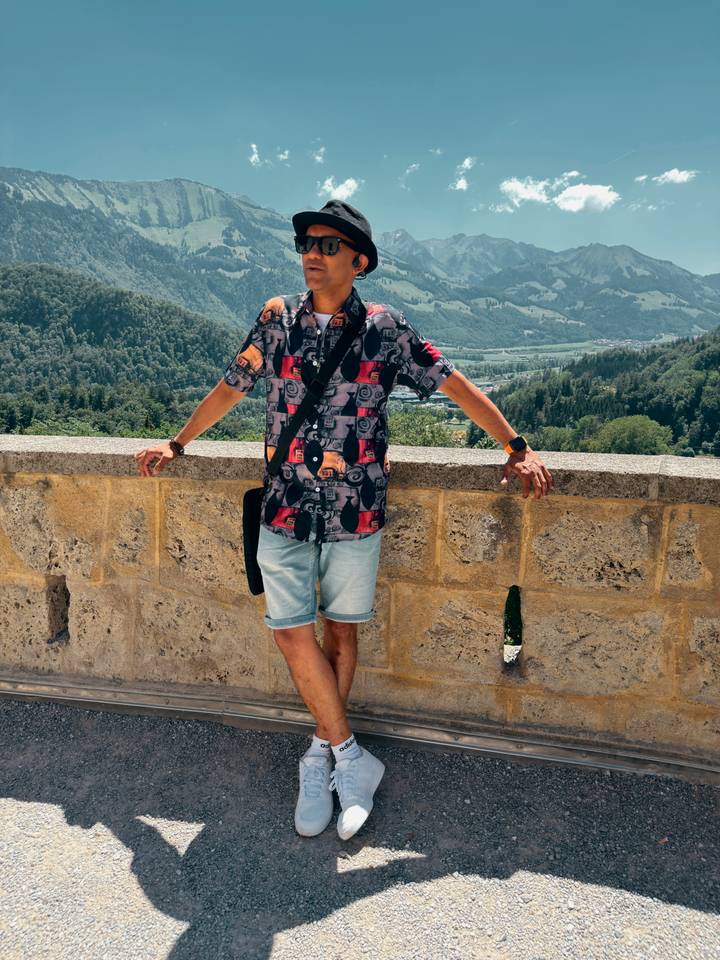 Traveller leaning casually on a stone wall with a lush green Swiss valley view below.