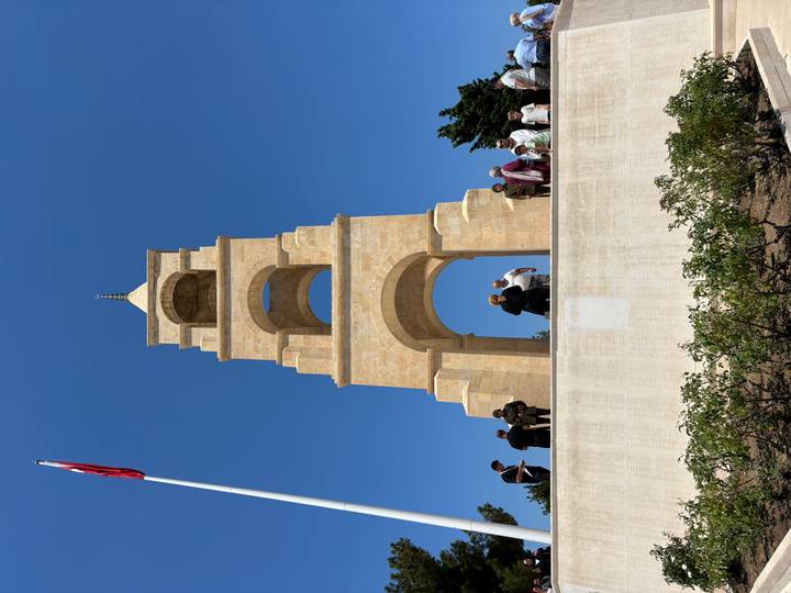 Stone bell tower memorial in Gallipoli rises against a clear blue sky with visitors at its base.