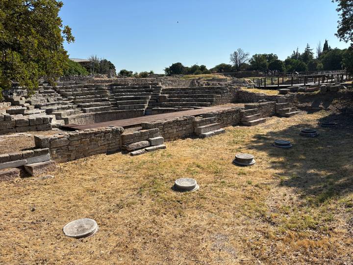 Stone remains of an ancient amphitheatre and surrounding ruins under late-afternoon light.